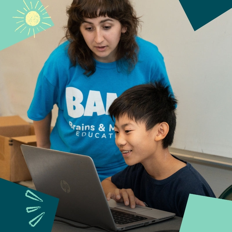 A BAM instructor helps a child working on a laptop.