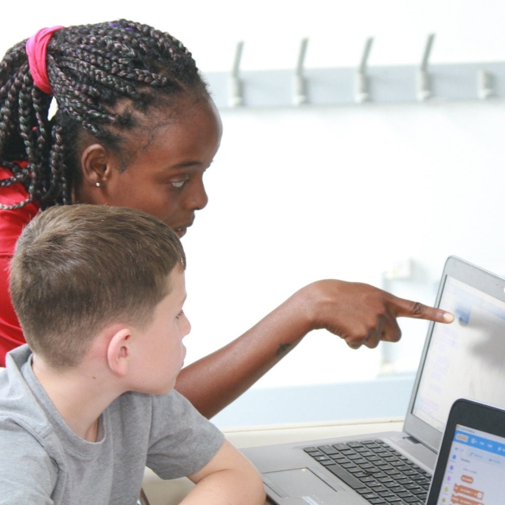 An instructor helps a child with a coding activity at a laptop.